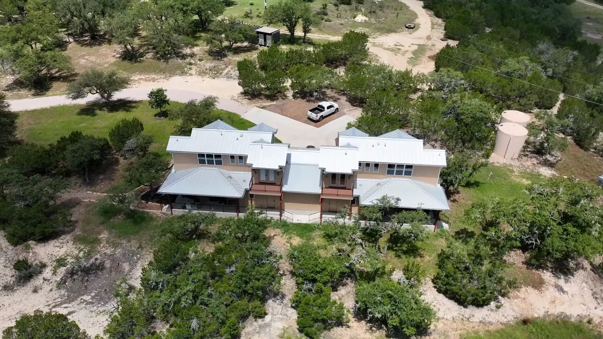 A ranch house seen from the drone mid-orbit, with live oaks and the drive around it